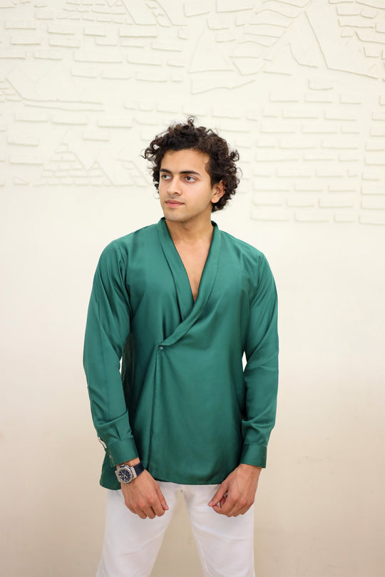 Man wearing a green shirt and white pants against a light textured wall