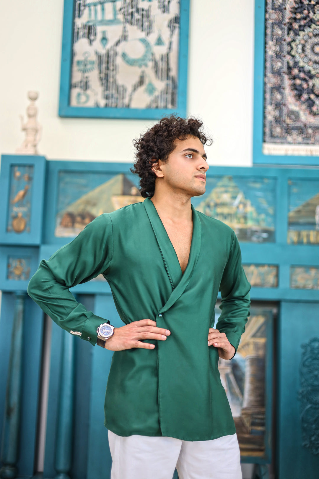 Man wearing a green shirt and white pants standing in front of a decorative blue wall.