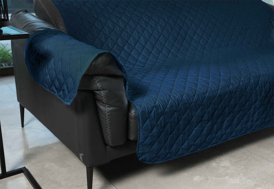 Blue quilted cover on a gray sofa in a room with a table and window.