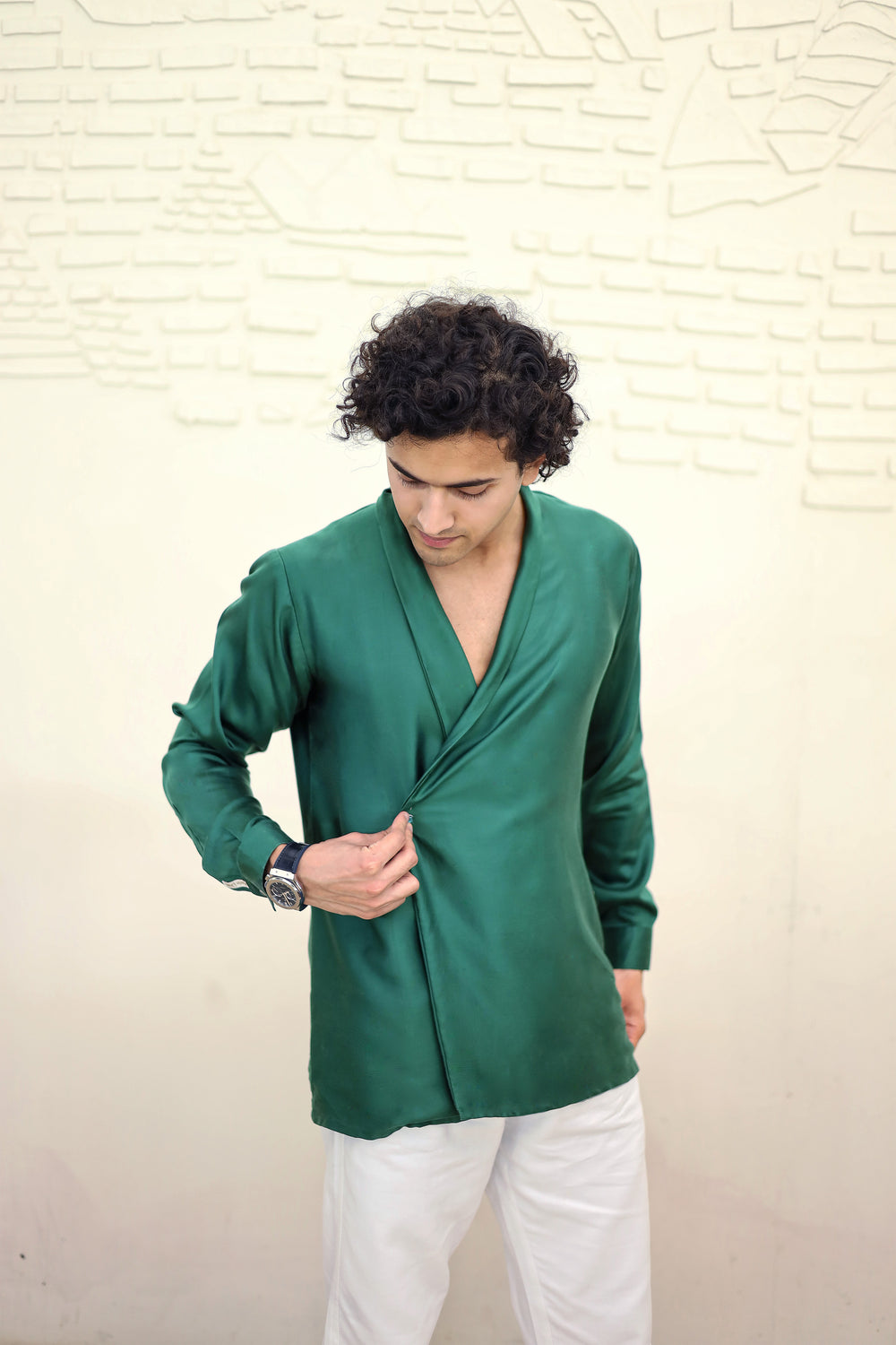 Man wearing a green wrap-style top against a textured beige wall
