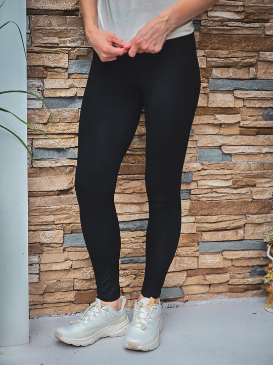 Person wearing black bamboo leggings and white sneakers standing against a stone wall.