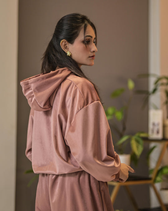 Woman wearing a pink tracksuit standing indoors with a neutral background