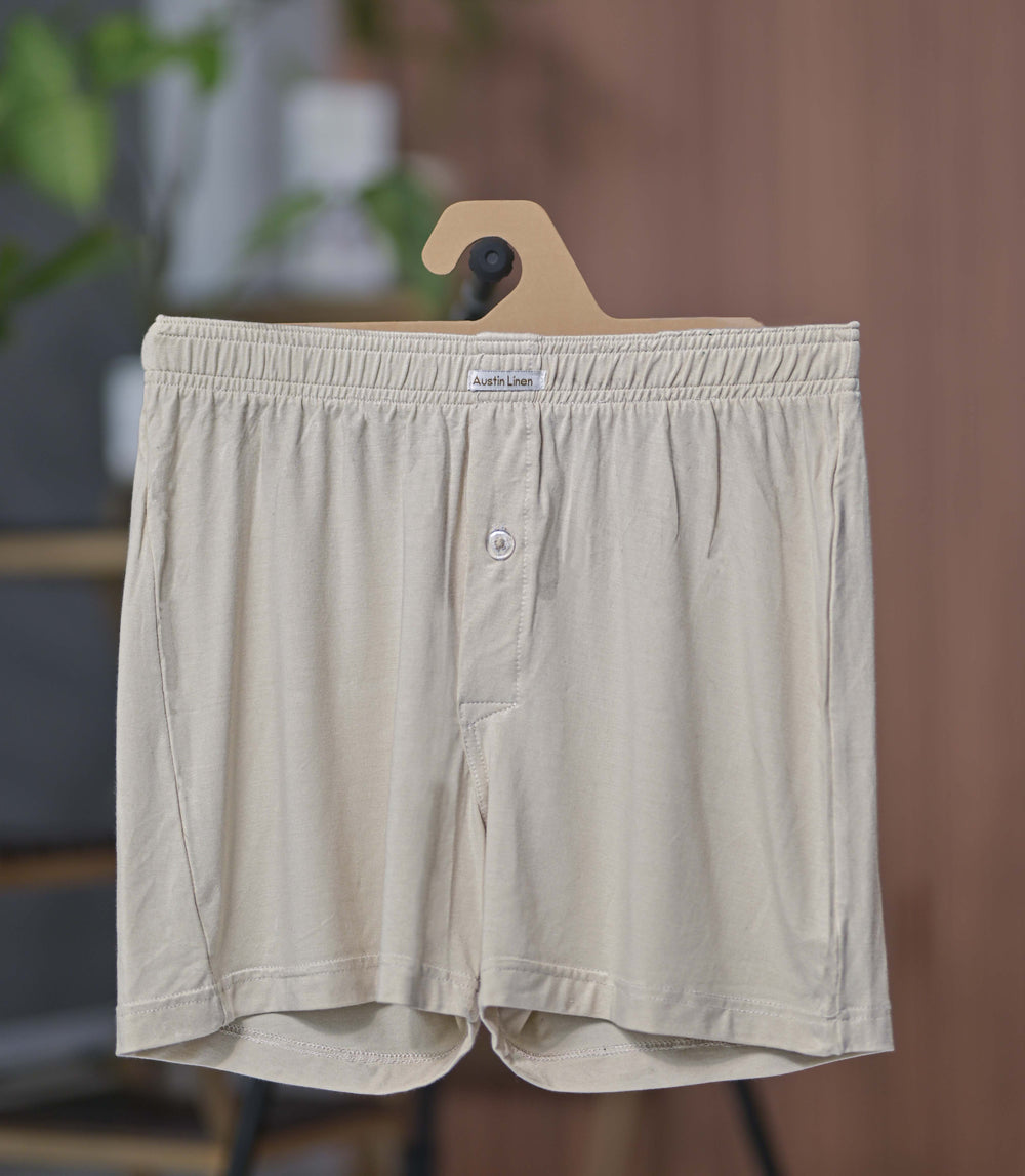 Beige boxer shorts on a wooden hanger against a blurred indoor background