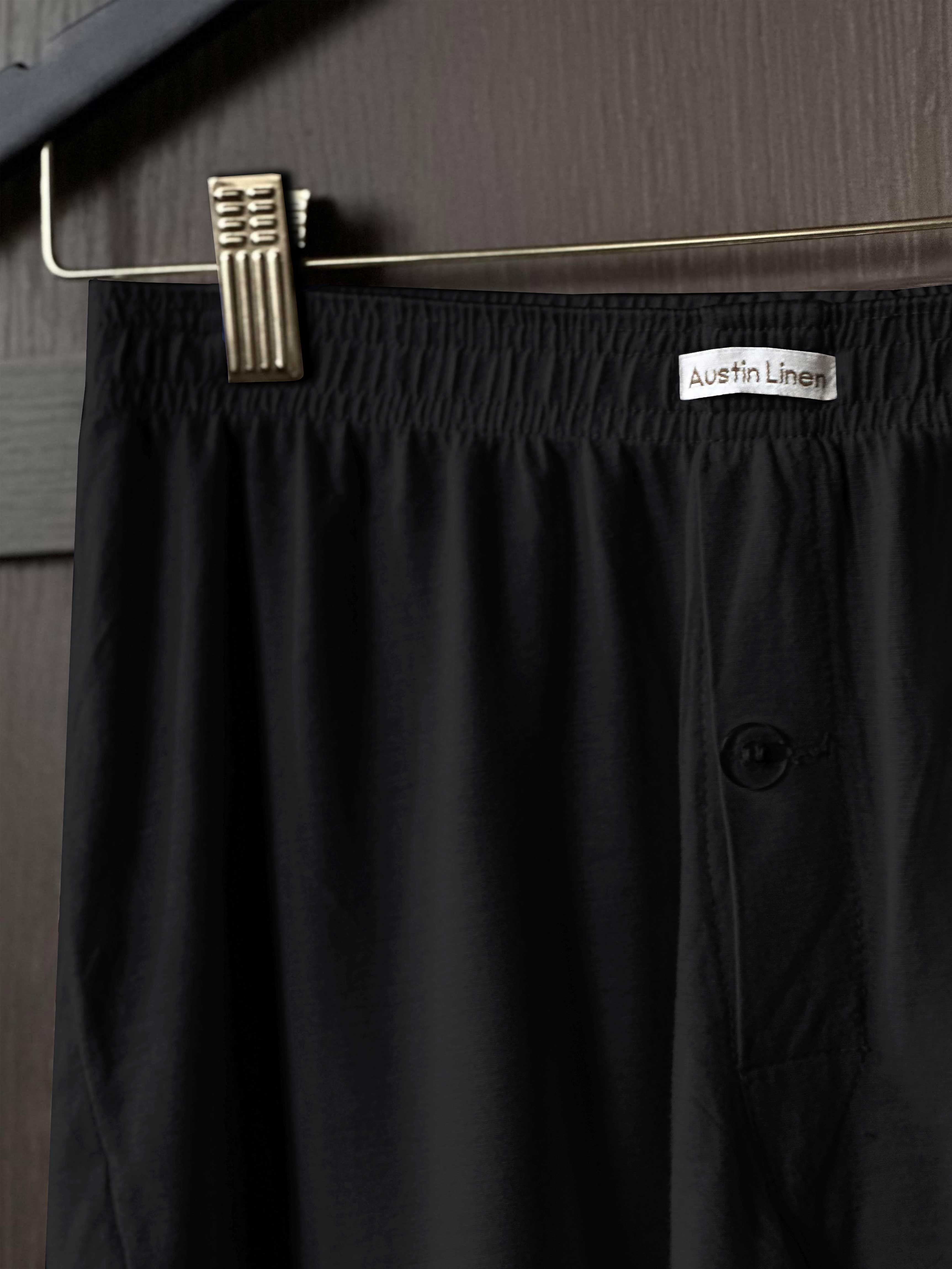 Black pajama pants on a hanger with 'Austin Linen' label against a gray background