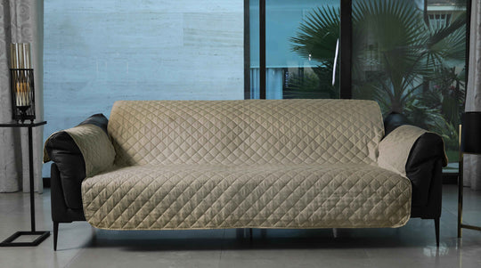 Beige quilted sofa cover on a dark sofa in a living room setting.