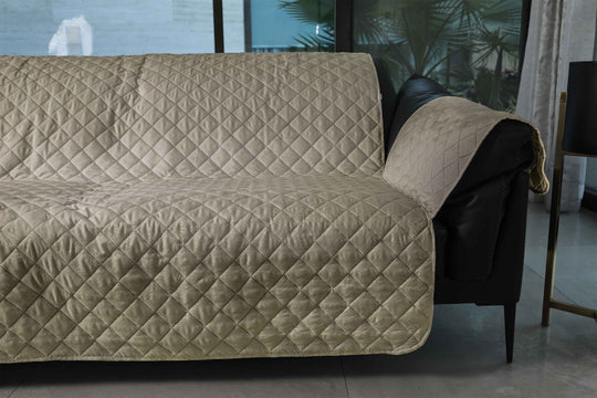 Beige quilted sofa cover on a black leather sofa in a living room setting.