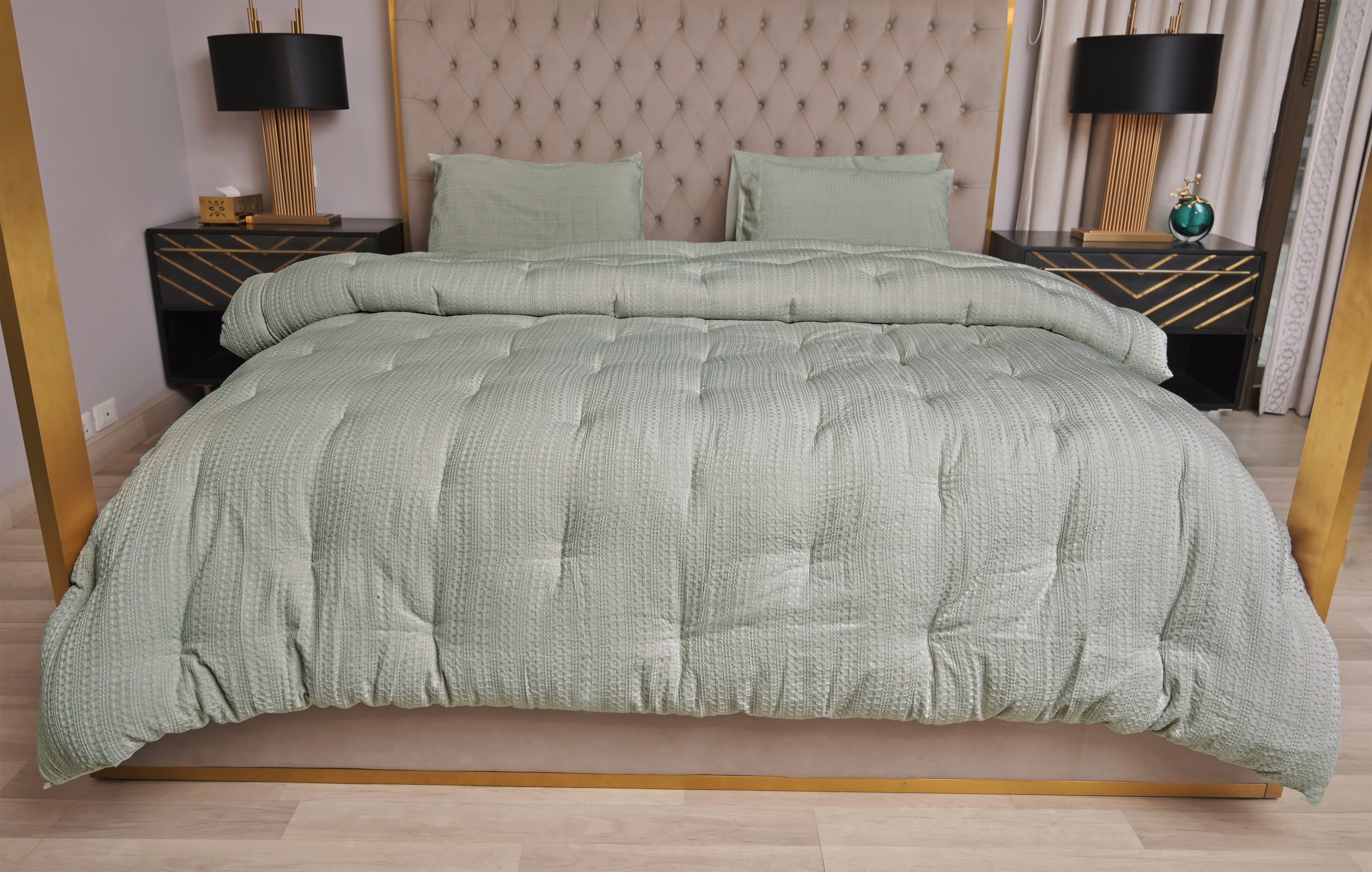 Green comforter on a bed with matching pillows in a bedroom setting.