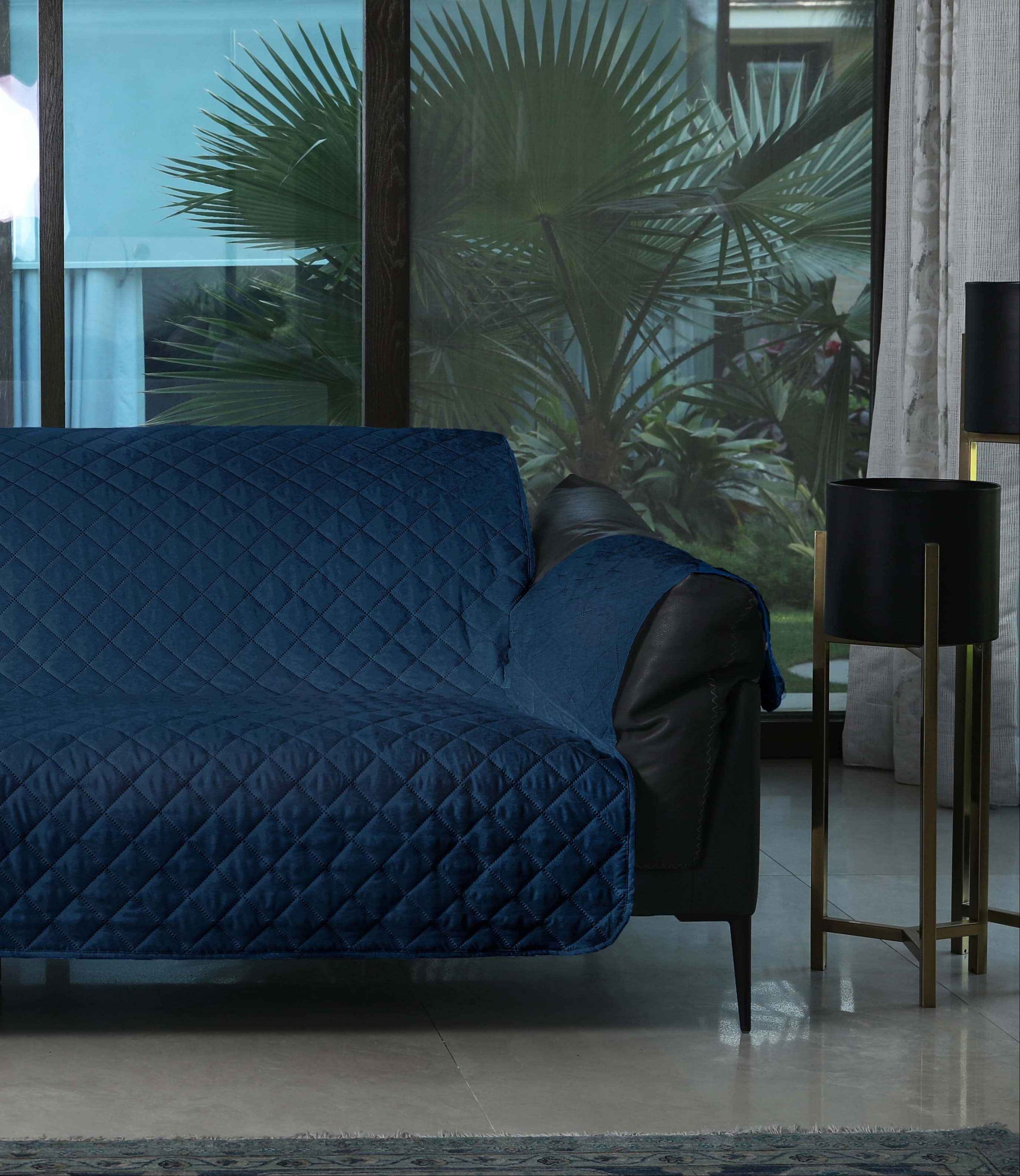 Blue quilted cover on a sofa in a modern living room with a glass door showing greenery.