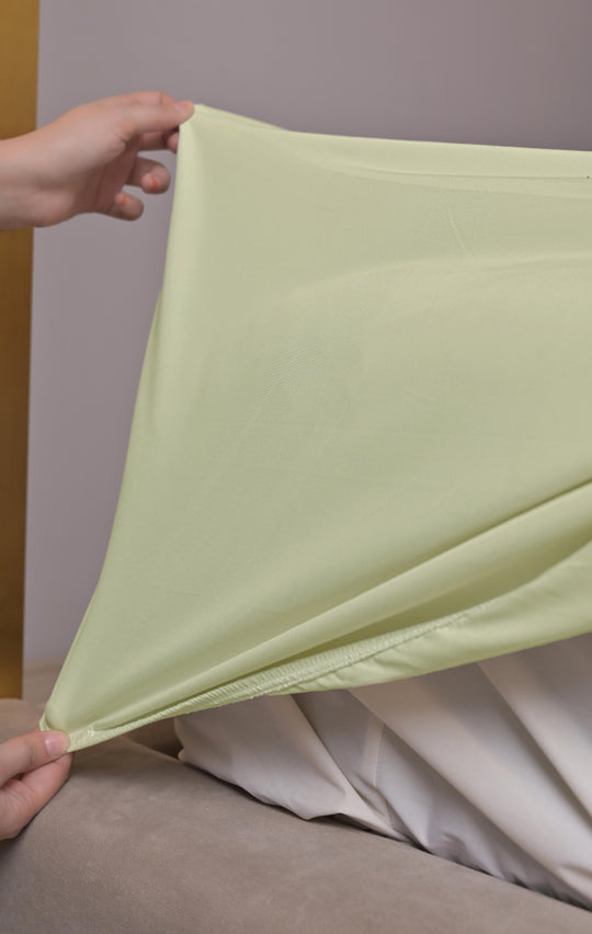 Person holding a light green fabric over a white sheet on a bed.