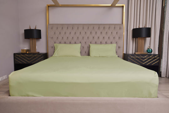 Bedroom with a bed featuring green bedding, a tufted headboard, and decorative lamps.