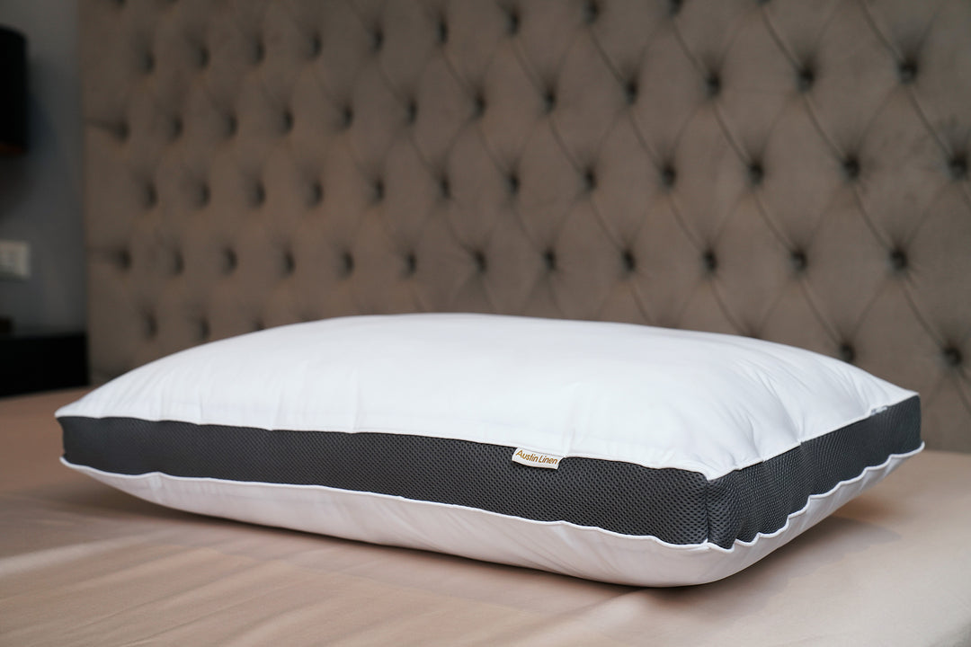 White pillow with gray accent on a bed against a tufted headboard.